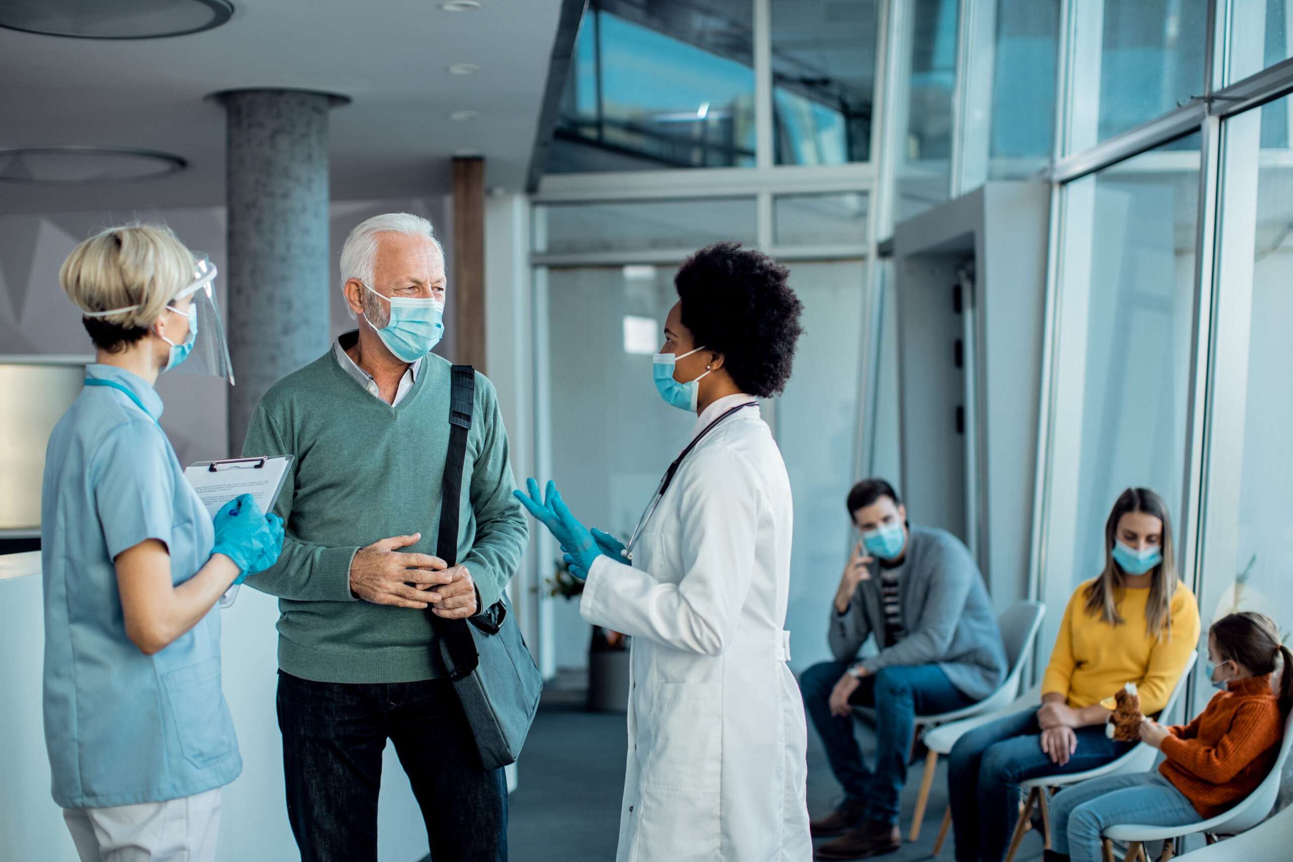 senior man with protective face mask talking to doctors at hospi